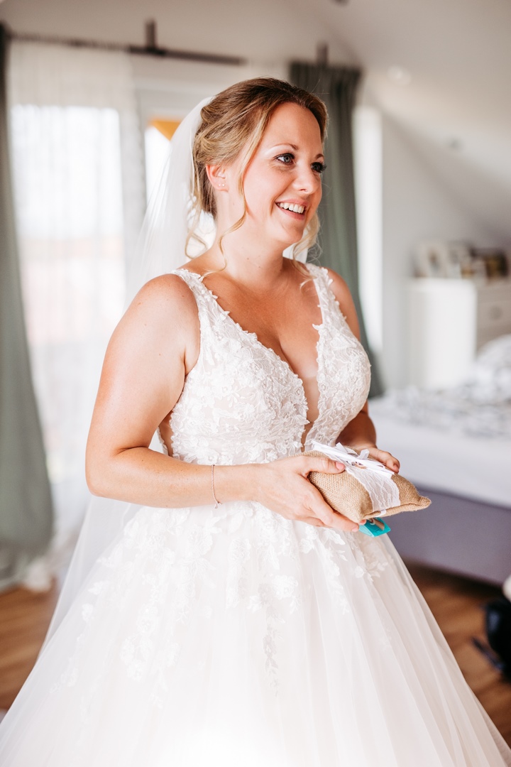 Lächelnde Braut im Spitzenkleid während der Hochzeitsvorbereitung