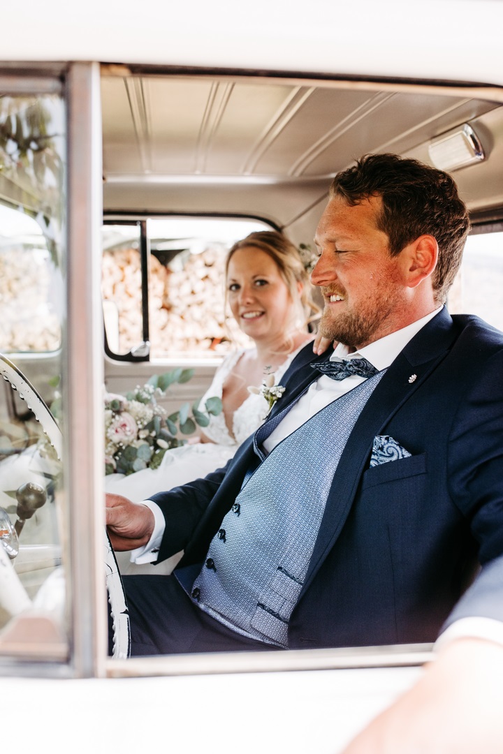 Brautpaar im weißen Hochzeitsauto durch das Seitenfenster gesehen