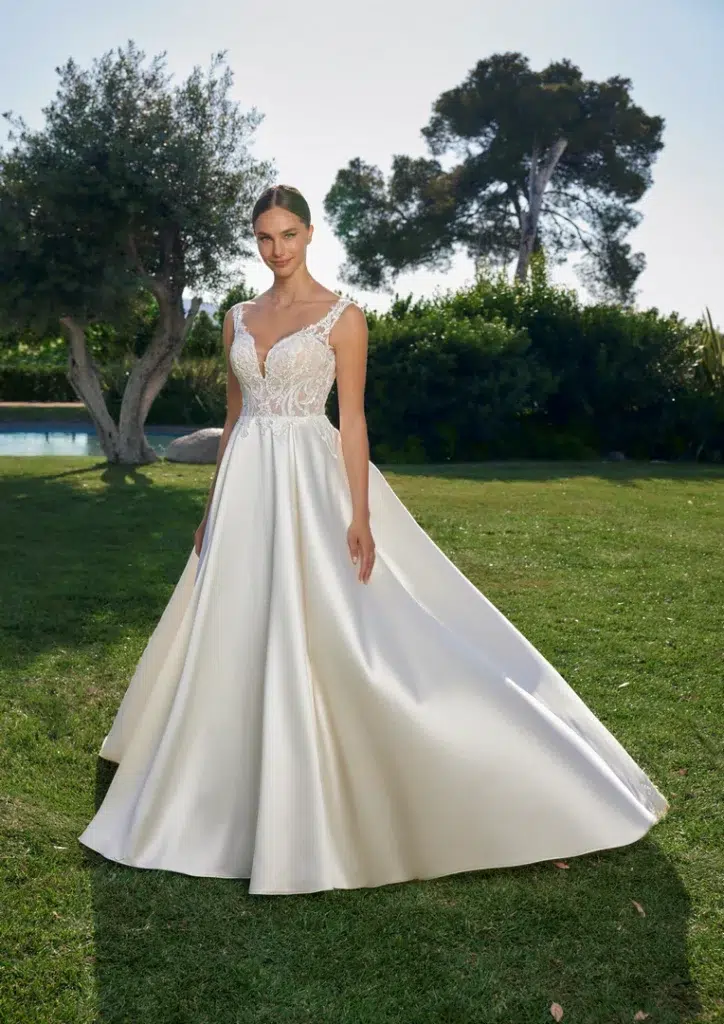 Brautkleid mit Spitzenoberteil, schmalen Trägern und glattem weitem Rock auf einer Wiese