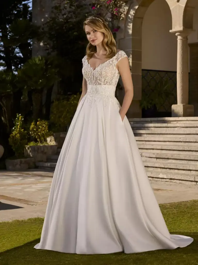 Brautkleid mit Spitzenoberteil, breiten Trägern und glattem Rock vor einer Treppe