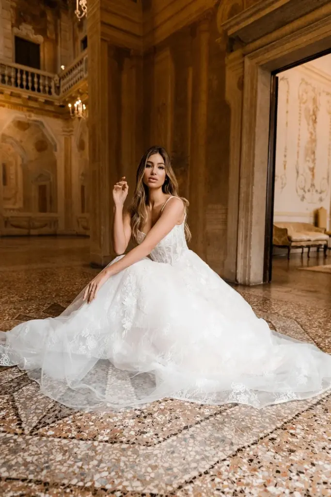 Sitzende Braut im Spitzenkleid mit weitem Tüllrock und Schleppe