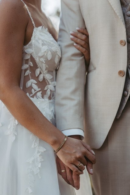 Detail von Brautkleid, hellem Anzug und den Händen des Brautpaars