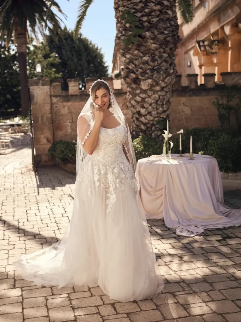 Brautkleid mit schmalen Trägern und floralen Applikationen vor einer Steinmauer