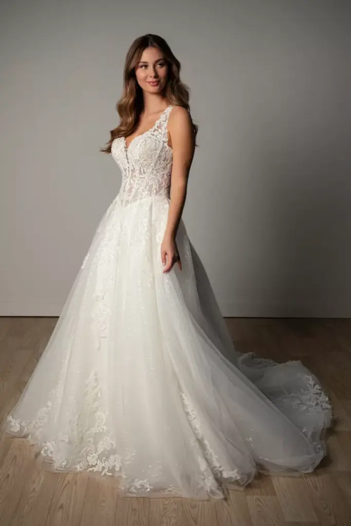 Brautkleid mit Spitzenoberteil, V-Ausschnitt und weitem Rock vor grauem Hintergrund