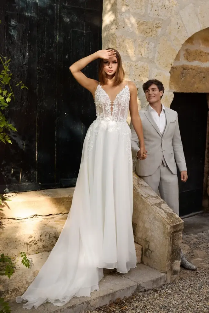 Braut in einem Kleid mit Spitzenoberteil und glattem Rock neben einer Begleitperson