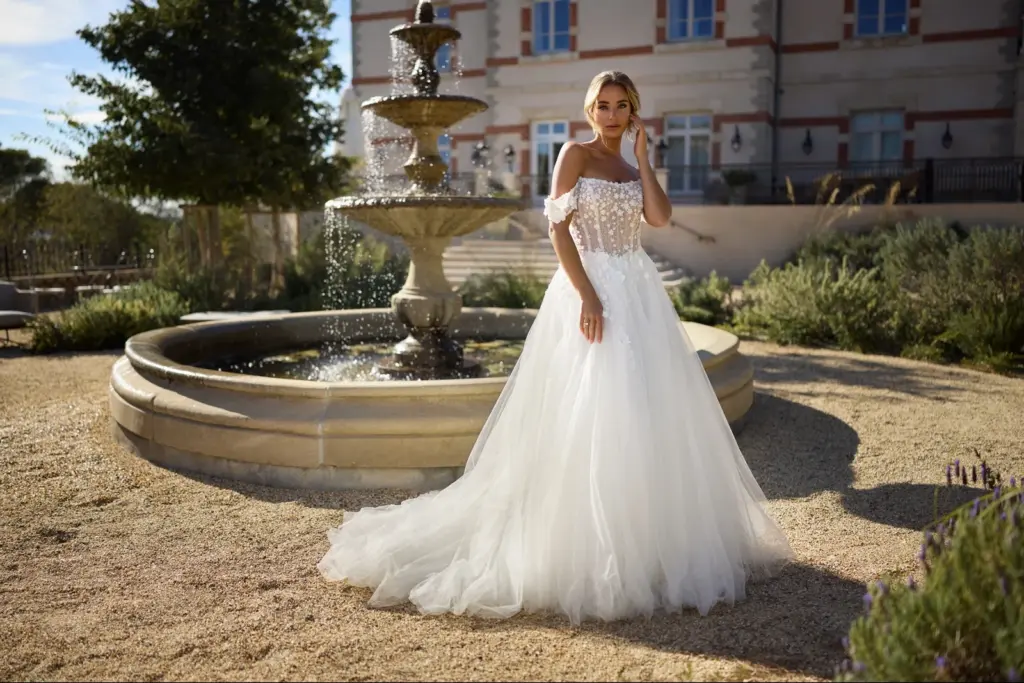 Brautkleid mit schulterfreien Ärmeln und weitem Tüllrock vor einem Brunnen