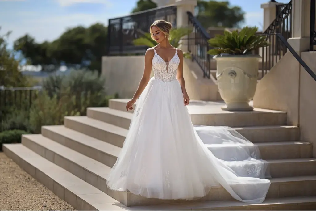 Brautkleid mit Spitzenoberteil, dünnen Trägern und weitem Tüllrock auf einer Treppe