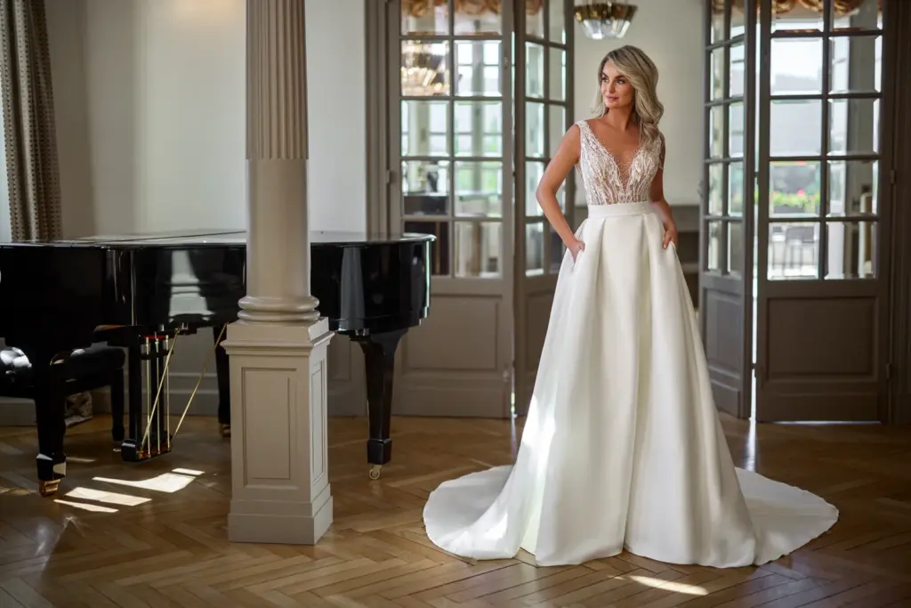 Brautkleid mit Spitzenoberteil und weitem glattem Rock neben einem Flügel